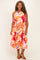 woman wearing a colorful floral plus-size dress with a halter neckline and tie waist, standing with a smile
