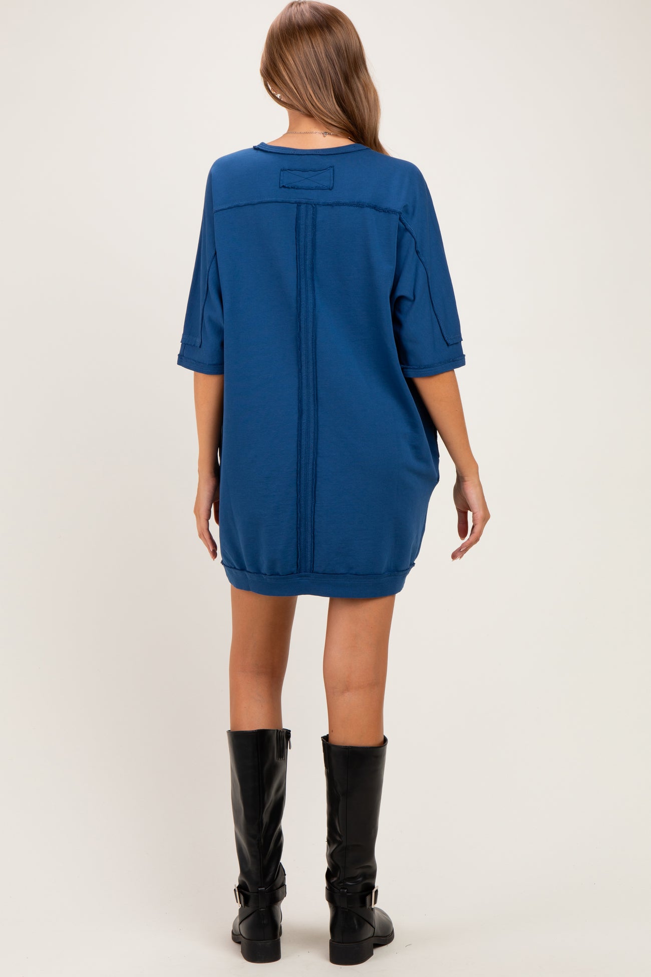 woman wearing a loose-fitting blue maternity dress with short sleeves and black knee-high boots, showing the back view