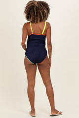 woman wearing a navy maternity one-piece swimsuit with colorful straps, showing her back and no visible baby bump