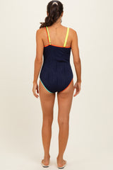 woman wearing a navy one-piece swimsuit with colorful strap details and a textured design, standing with her back to the camera