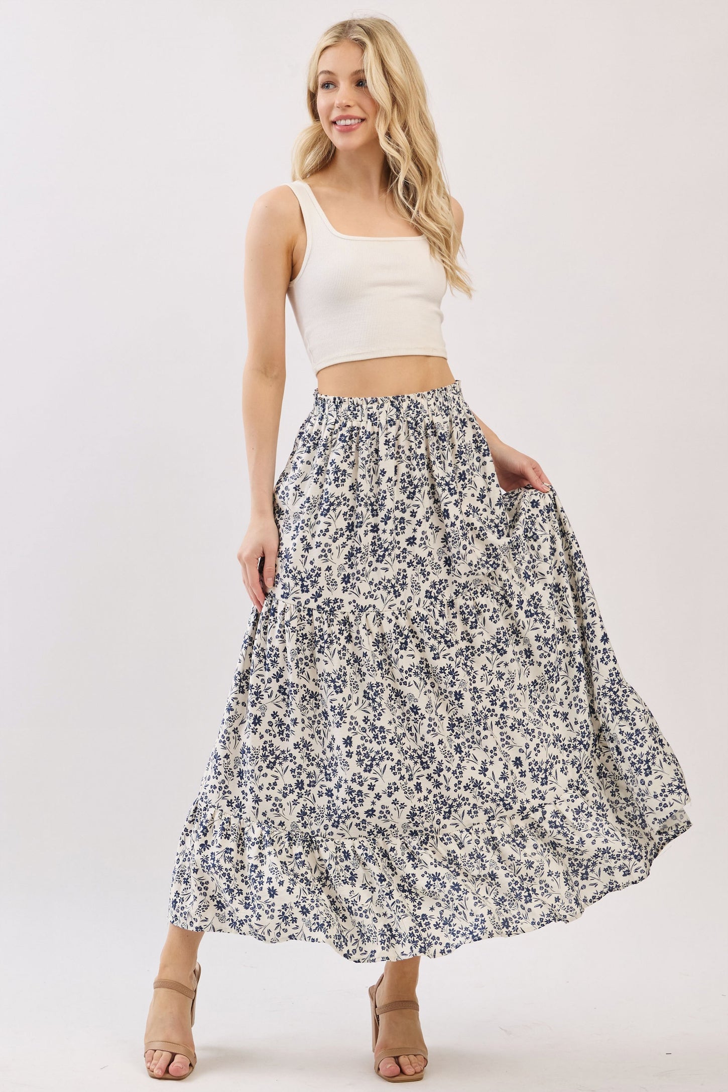 woman wearing a white crop top and a flowing blue floral print maxi skirt, smiling with hands in pockets