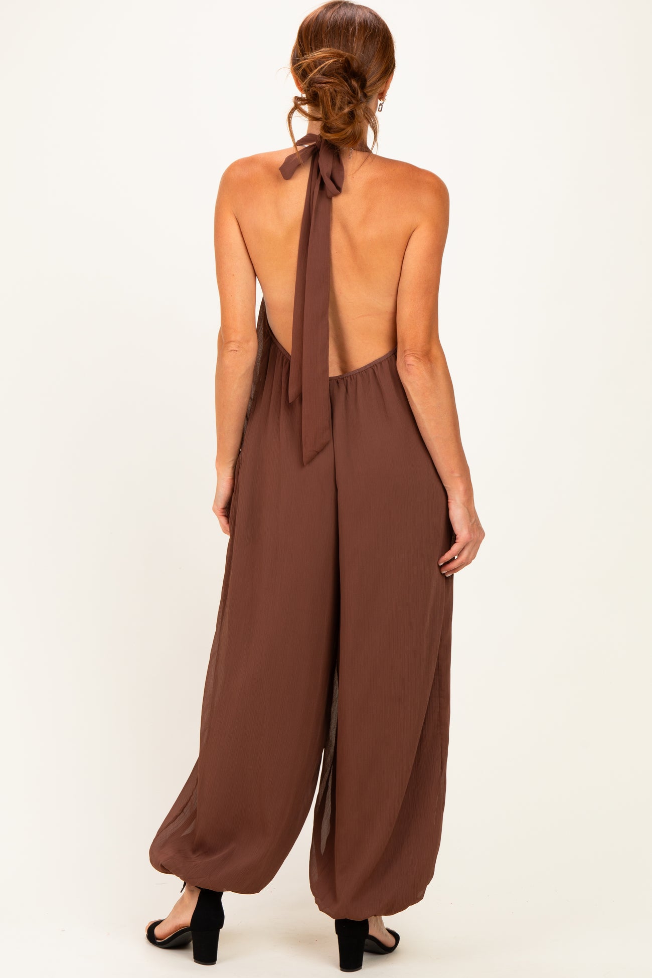 woman wearing a brown backless jumpsuit with a halter tie detail and wide-leg pants
