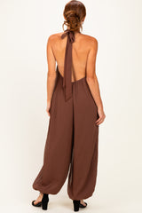 woman wearing a brown backless jumpsuit with a halter tie detail and wide-leg pants