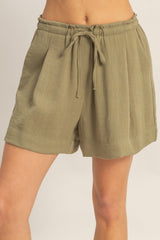 woman wearing olive green high-waisted pleated shorts with a drawstring waistband