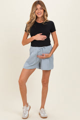 woman wearing a black fitted t-shirt and light blue maternity shorts, holding her baby bump