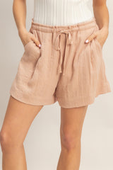 woman wearing blush pink linen shorts with an elastic waistband and pockets, featuring a relaxed fit