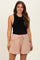 woman wearing a black sleeveless top and light pink maternity shorts with an elastic waist and tie detail, smiling