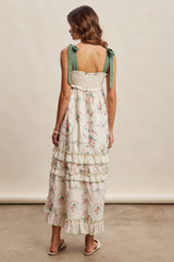 woman wearing a white floral maxi dress with tiered ruffles and green bow straps, shown from the back