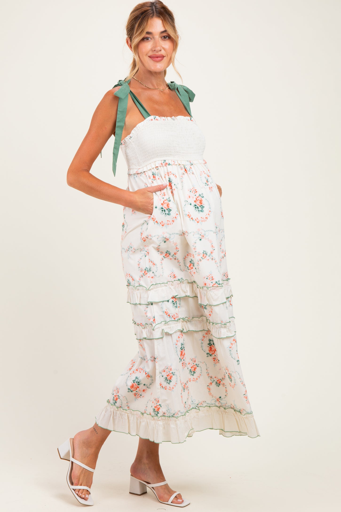 woman wearing a floral maternity maxi dress with tiered ruffles and green ribbon straps, showcasing her baby bump