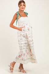 woman wearing a floral maternity maxi dress with tiered ruffles and green ribbon straps, showcasing her baby bump