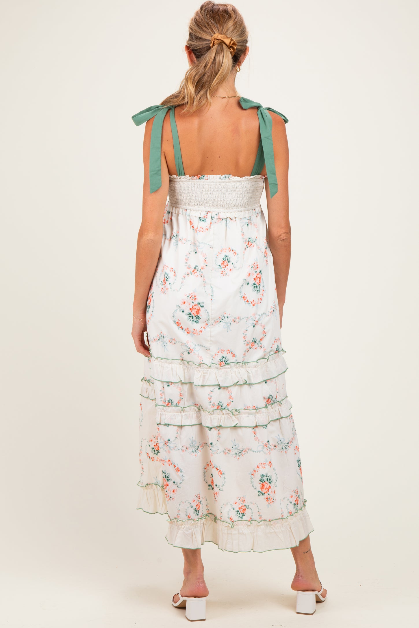 woman wearing a floral maternity maxi dress with green tie straps and tiered ruffles, showing a baby bump from the back