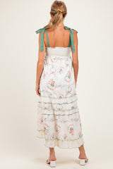 woman wearing a floral maternity maxi dress with green tie straps and tiered ruffles, showing a baby bump from the back