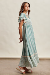 woman wearing a teal floral maxi dress with ruffled short sleeves and a tiered hem, paired with wedge sandals