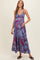 woman wearing a blue and red printed maternity maxi dress, holding her baby bump