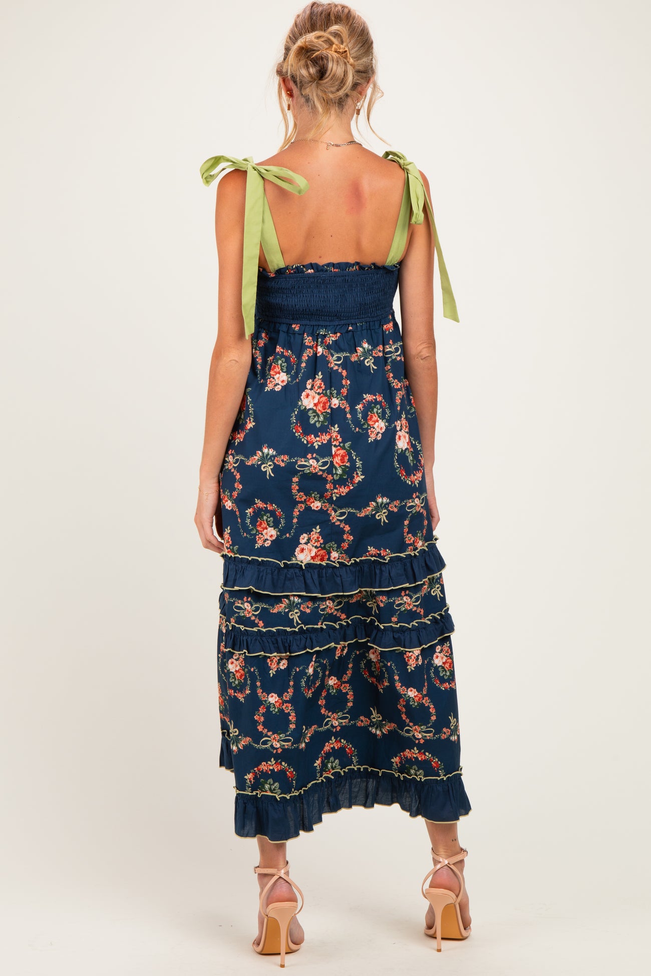 woman wearing a navy blue floral maternity maxi dress with ribbon tie straps and tiered ruffles, showing her baby bump