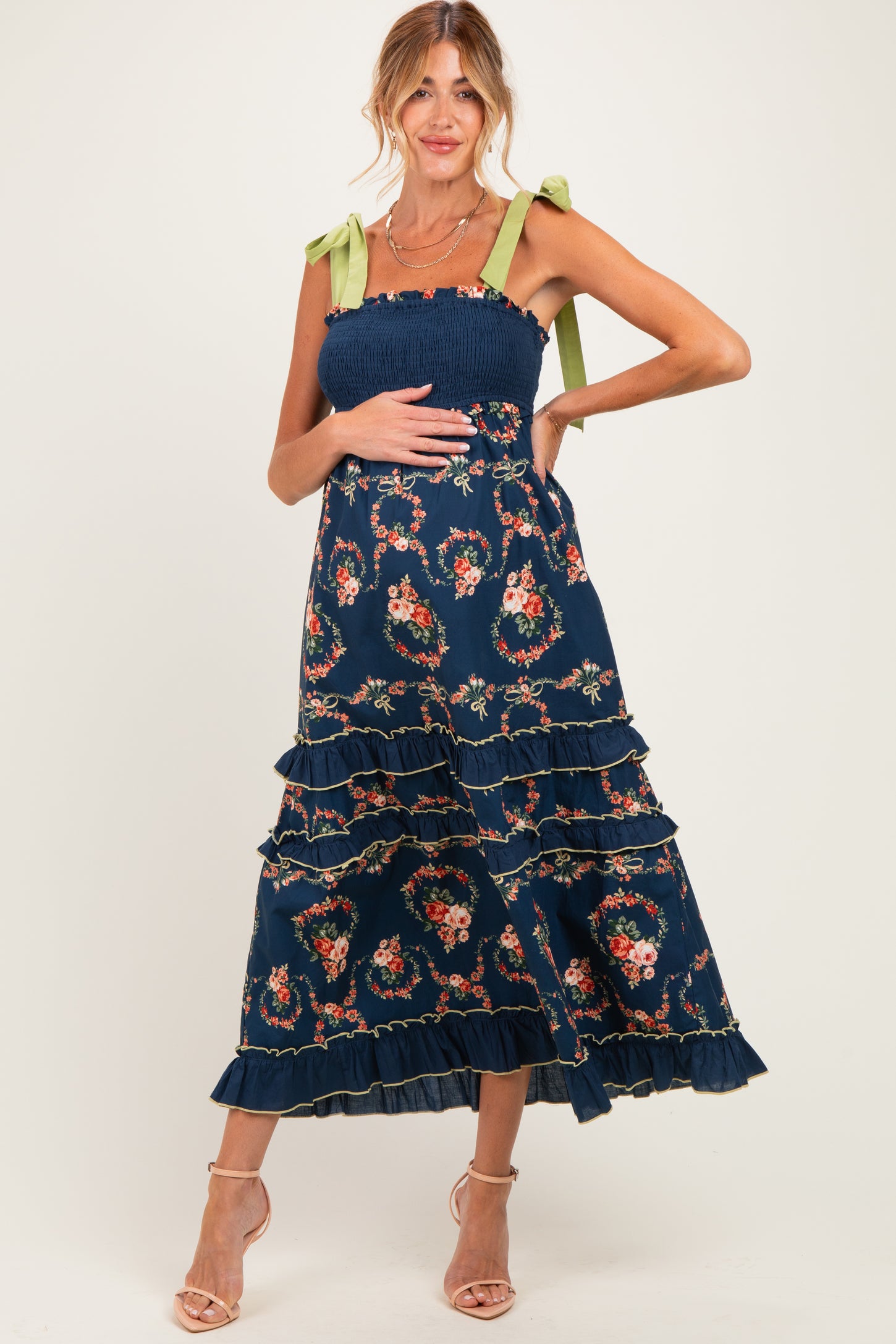 woman wearing a navy floral maternity dress with ruffled tiers and green tie straps, showcasing her baby bump