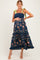 woman wearing a navy floral maternity dress with ruffled tiers and green tie straps, showcasing her baby bump
