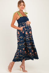 woman wearing a navy blue floral maternity maxi dress with ruffled layers and green shoulder straps, showing her baby bump