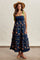 woman wearing a navy blue floral maxi dress with ruffled tiers and green tie straps, accessorized with a straw hat
