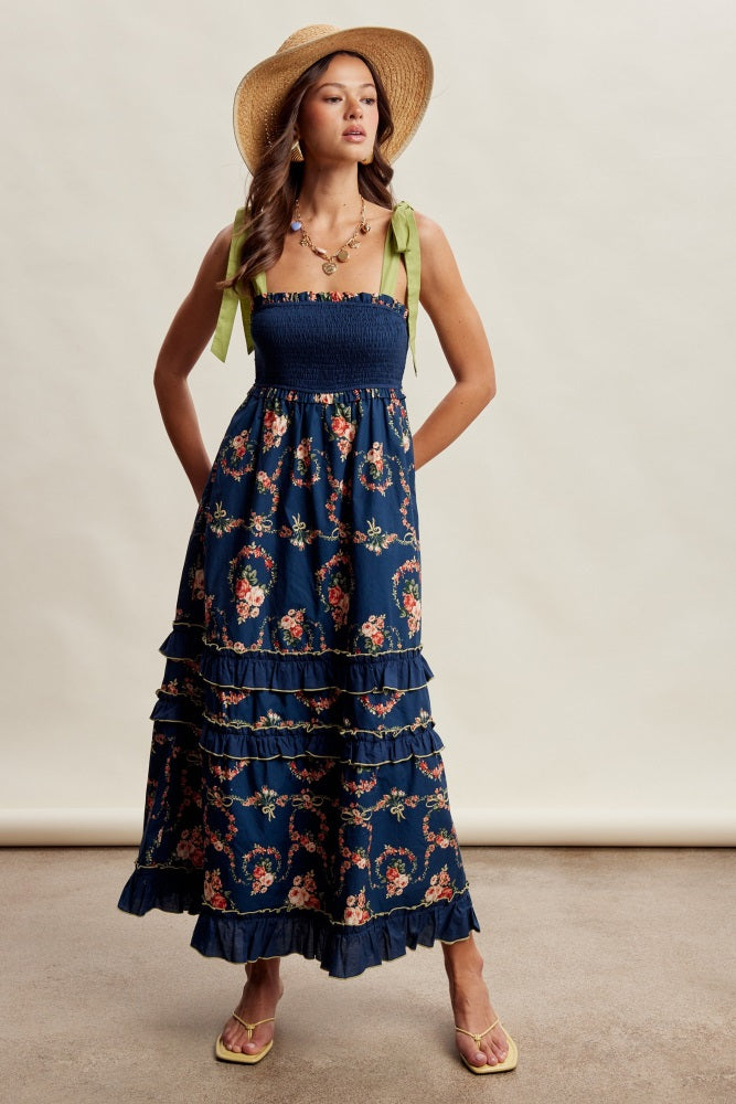 woman wearing a navy floral maxi dress with ruffles and green bow straps, styled with a straw hat