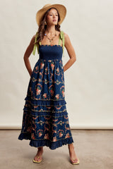 woman wearing a navy floral maxi dress with ruffles and green bow straps, styled with a straw hat