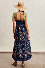 woman wearing a navy floral maxi dress with smocked bodice and ruffled layers, styled with a wide-brim straw hat
