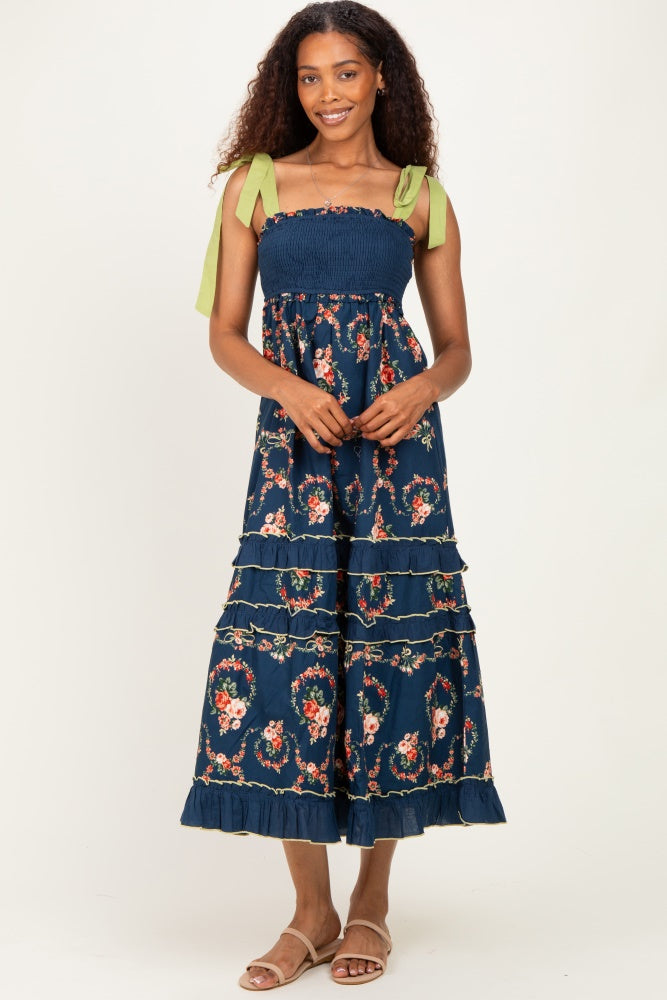 woman wearing a navy floral maxi dress with smocked bodice and green tie straps, standing and smiling