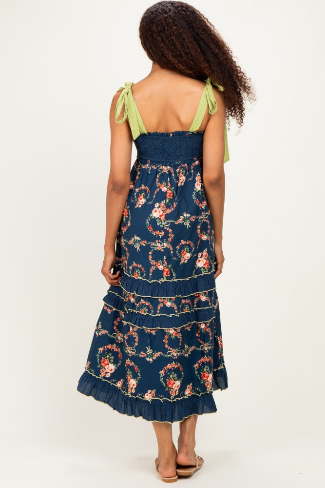 woman wearing a navy floral maxi dress with green tie-shoulder straps and ruffled hem, viewed from the back