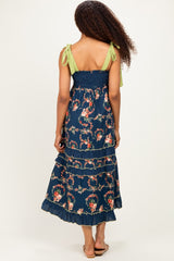 woman wearing a navy floral maxi dress with green tie-shoulder straps and ruffled hem, viewed from the back