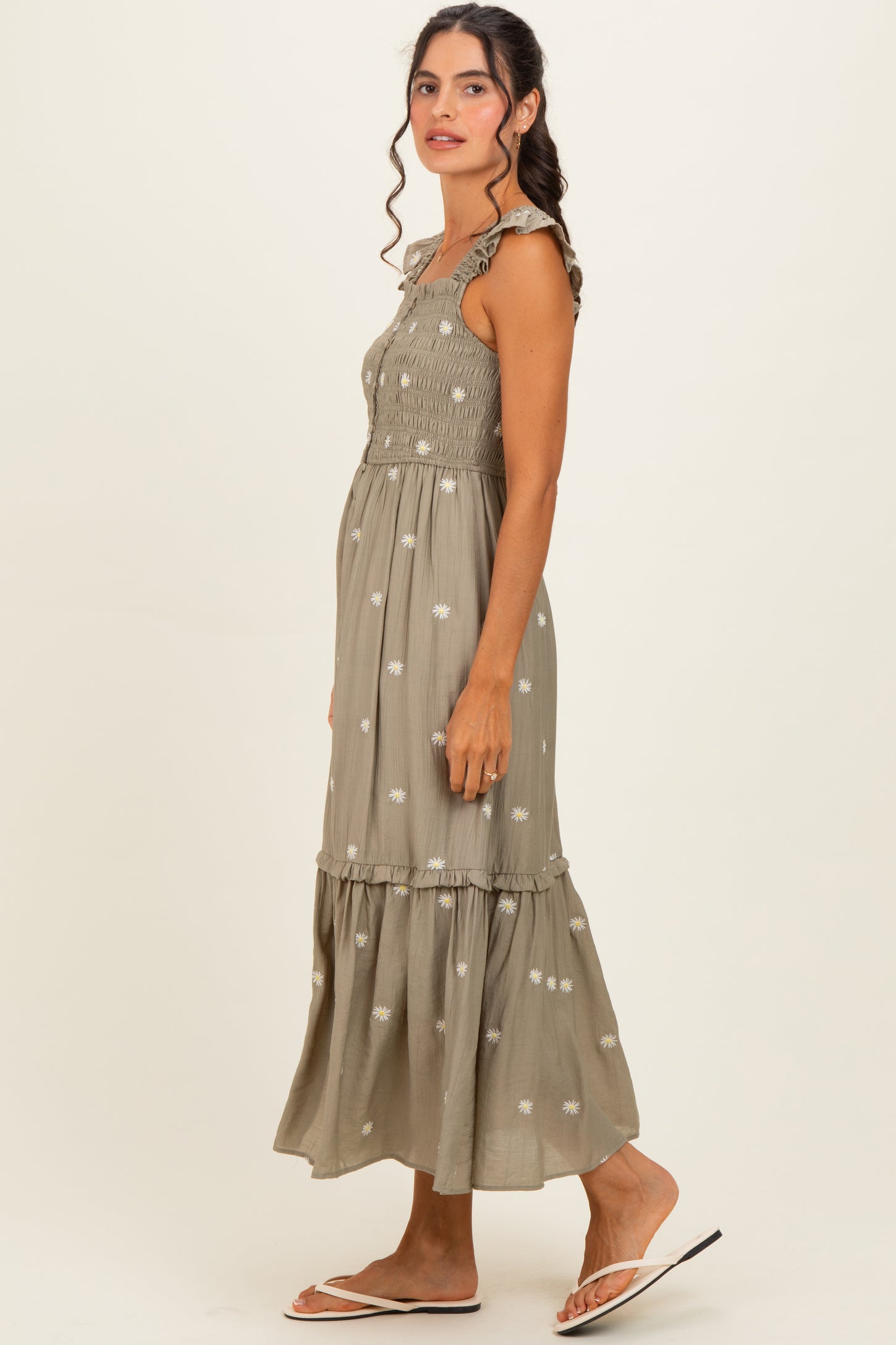 woman wearing a sage green sleeveless maxi dress with embroidered flowers and a tiered skirt, standing sideways
