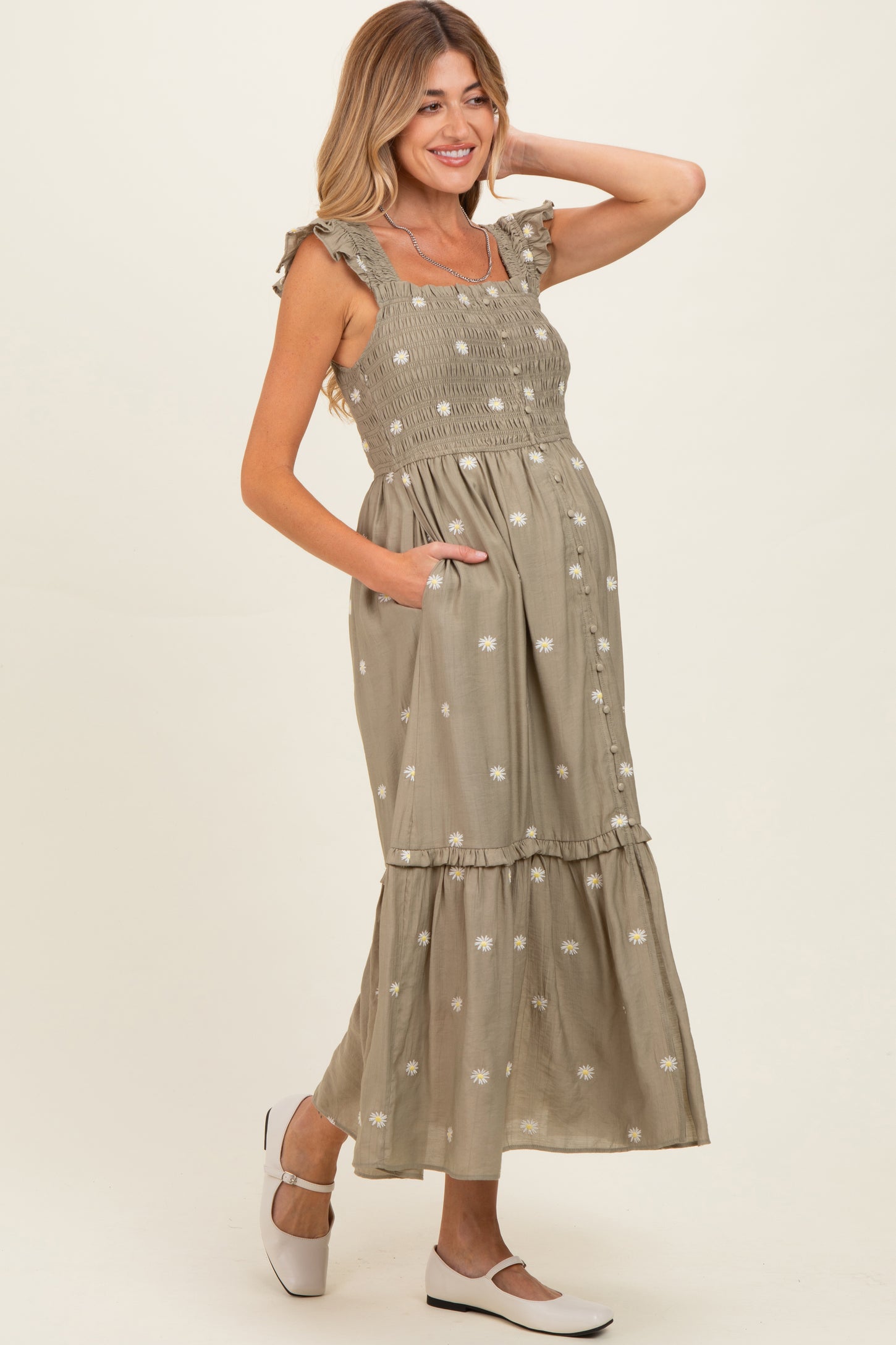 woman wearing a sage green maternity maxi dress with ruffled sleeves, smocked bodice, floral embroidery, and pockets
