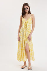 woman wearing a yellow floral maxi dress with a tied front and buttons, posing with sunglasses and sandals