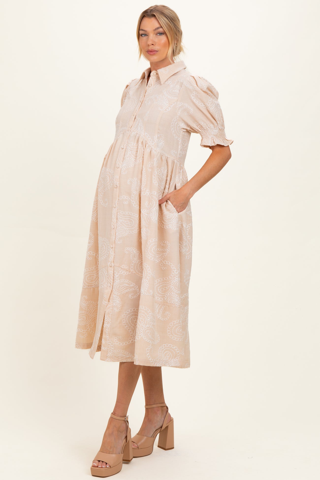 woman wearing a light peach paisley print maternity dress with short puff sleeves and a button-down front, baby bump visible
