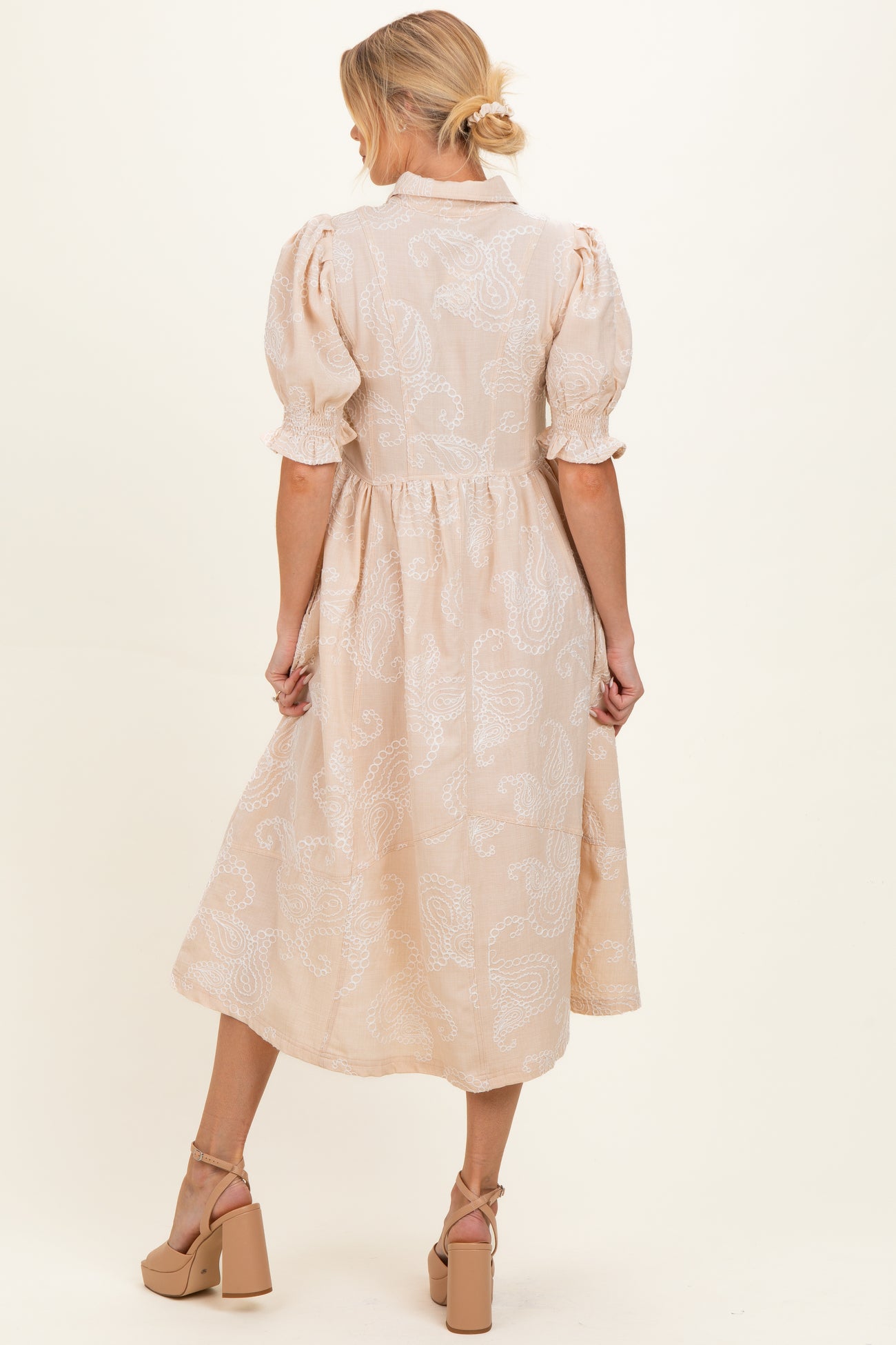 woman wearing a beige maternity dress with puff sleeves and a flowing skirt, showing a baby bump from the back