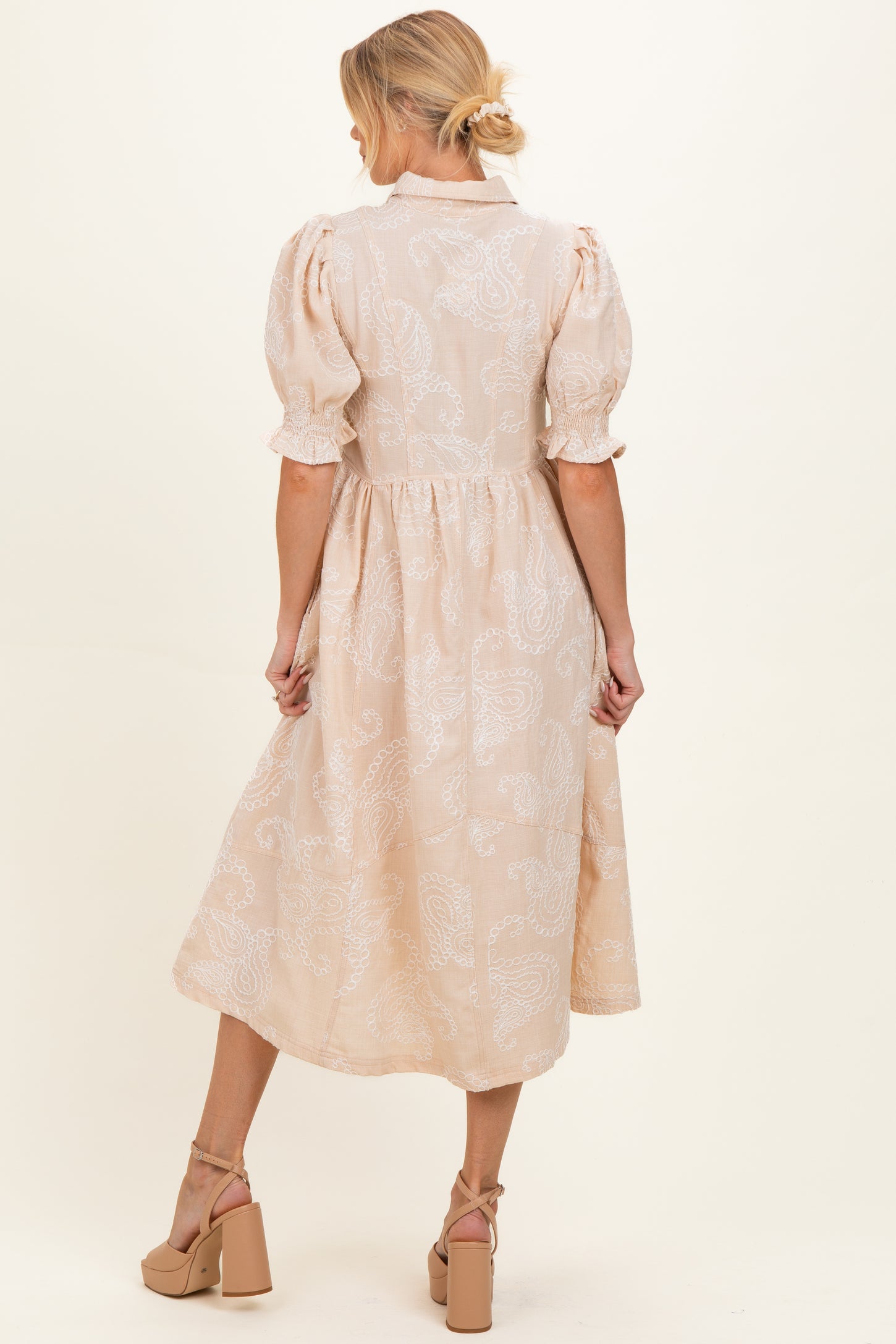 woman wearing a beige maternity dress with puff sleeves and a flowing skirt, showing a baby bump from the back