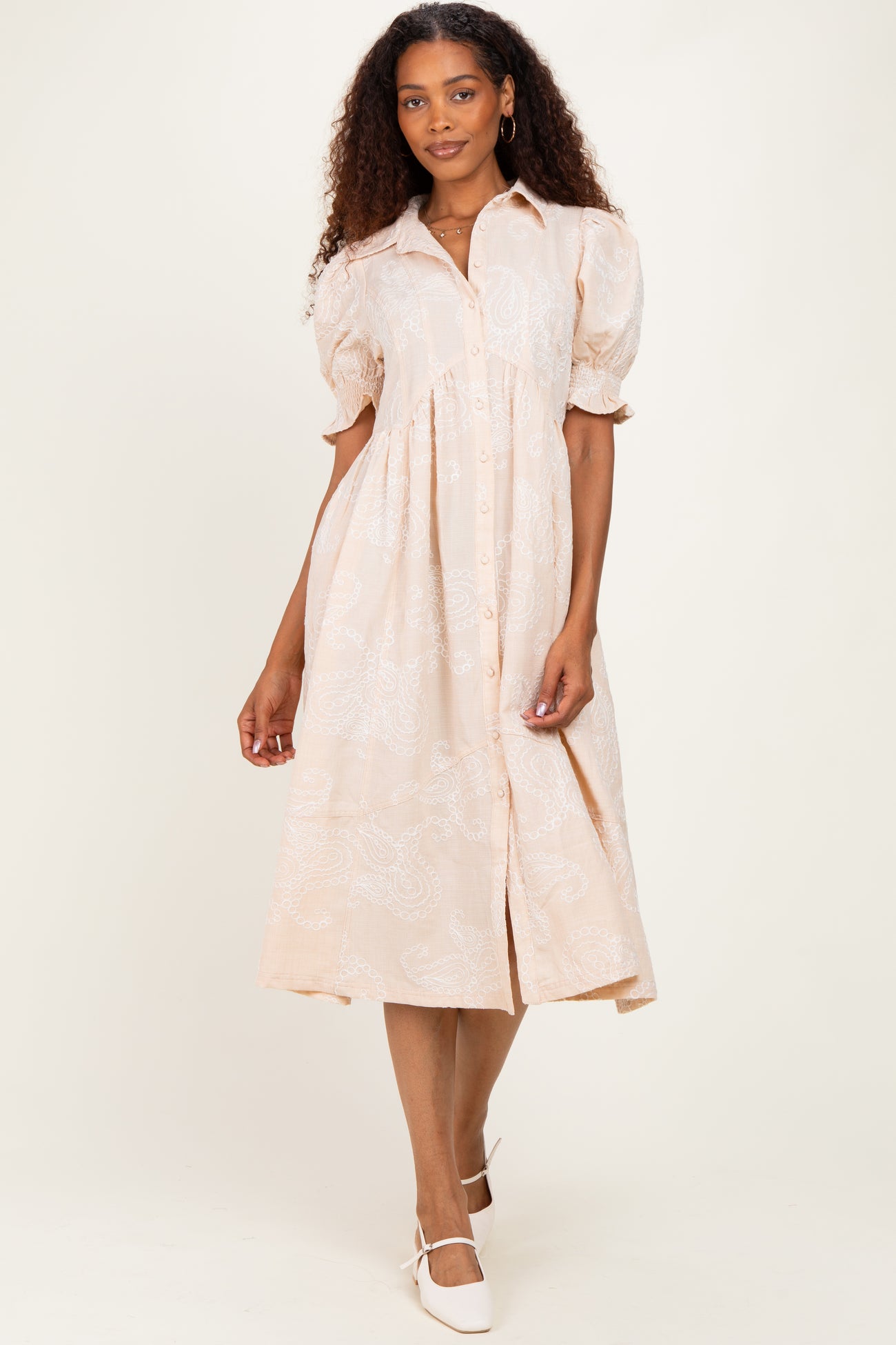 woman wearing a blush pink midi dress with puff sleeves and button details, standing against a neutral background