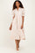 woman wearing a blush pink midi dress with puff sleeves and button details, standing against a neutral background