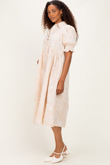 woman wearing a light peach button-up midi dress with puff sleeves and a paisley pattern, styled with white heels