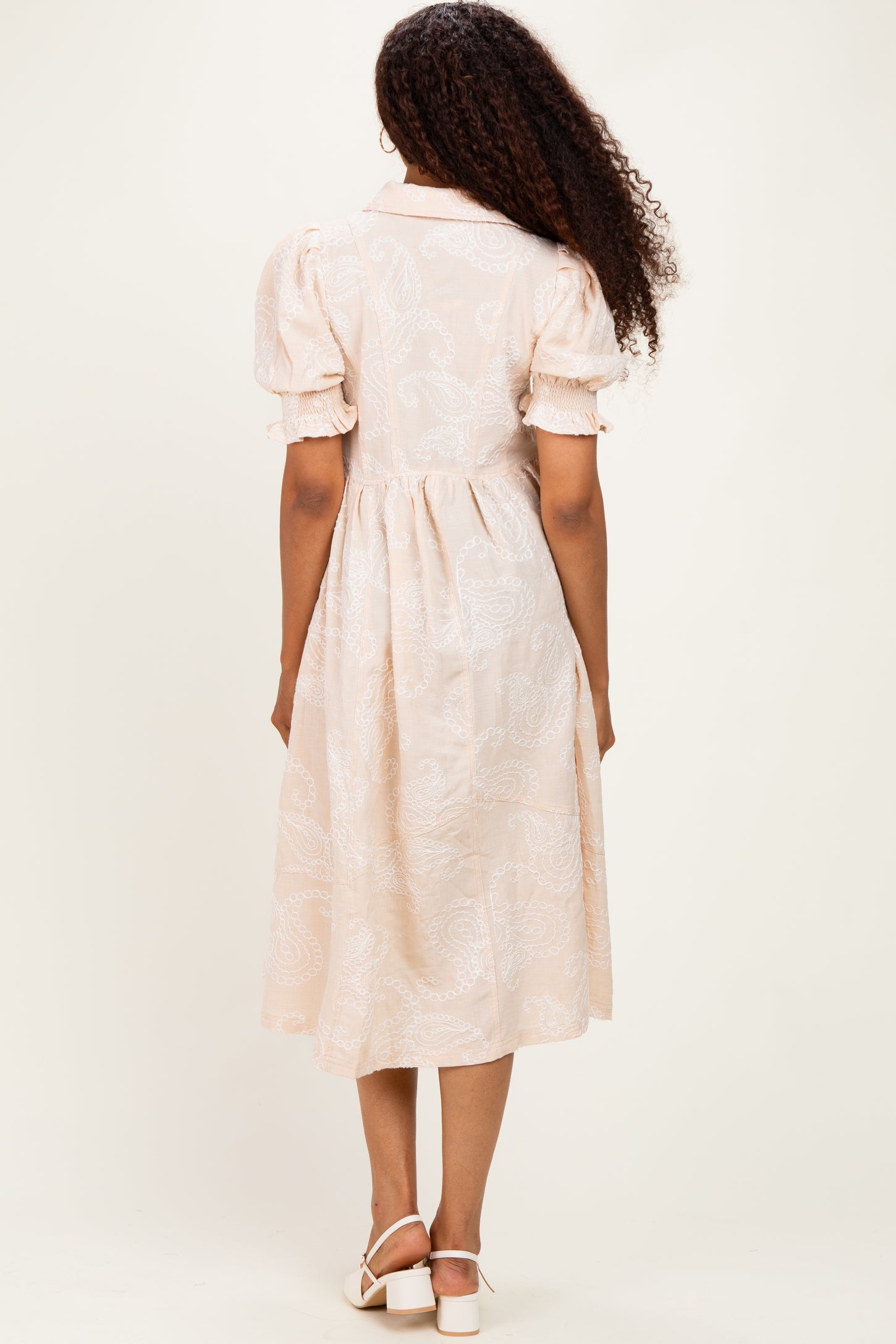 woman wearing a light pink midi dress with short puff sleeves and a belted waist, shown from the back