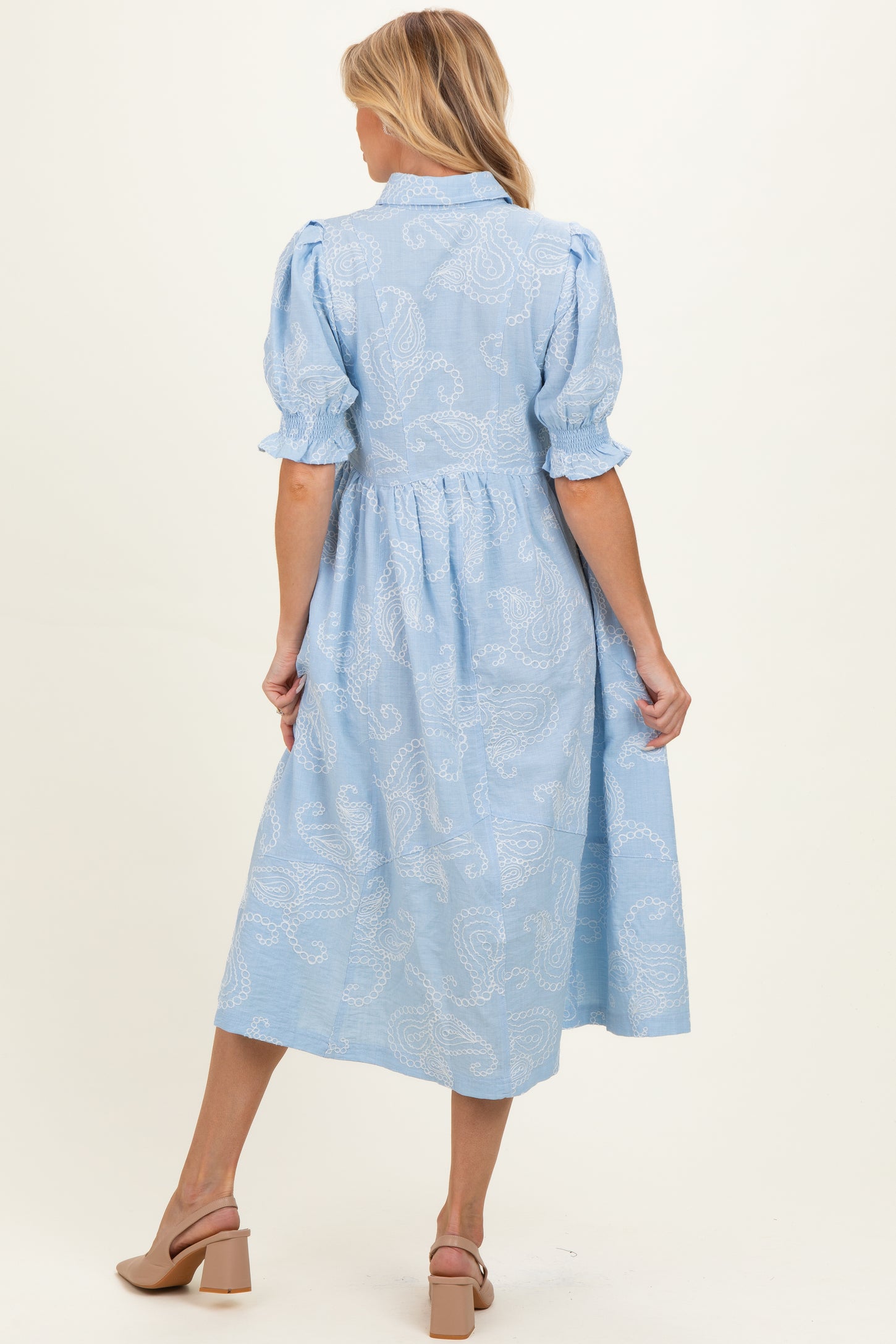 woman wearing a light blue maternity dress with puff sleeves and paisley print, showing a baby bump from the back