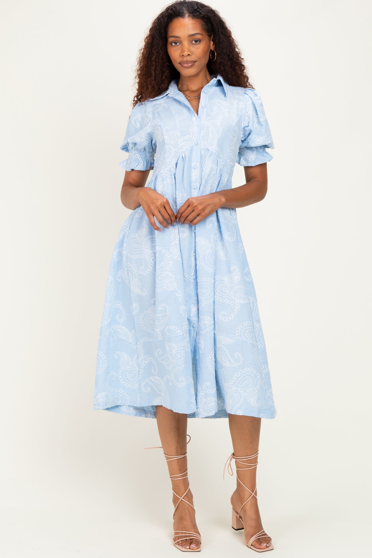 woman wearing a light blue paisley print button-up midi dress with short puff sleeves and a cinched waist
