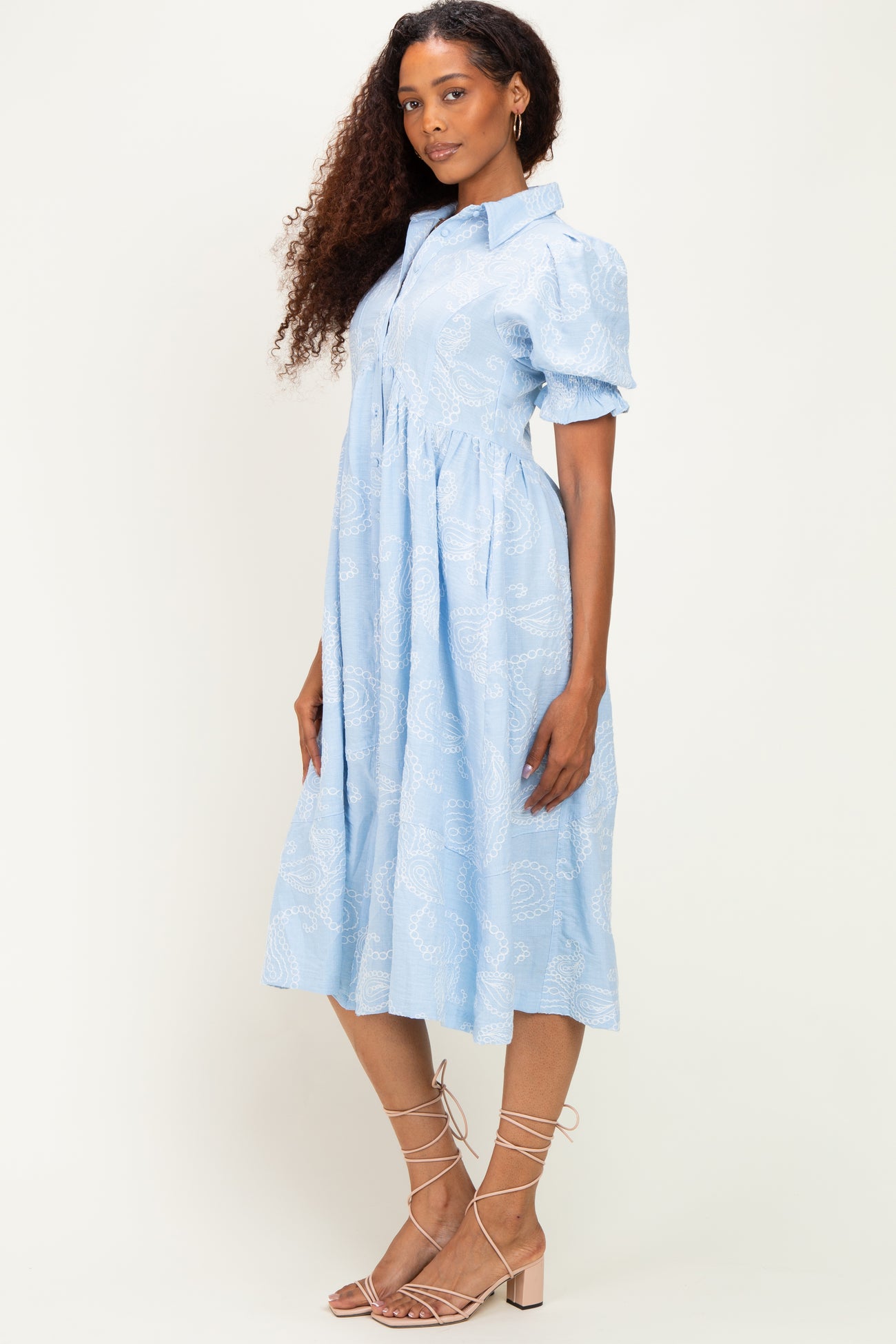 woman wearing a light blue midi shirt dress with puff sleeves and paisley print, standing sideways