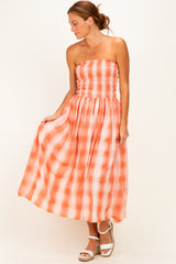 woman wearing an orange and white plaid strapless maxi dress with a smocked bodice and flowing skirt