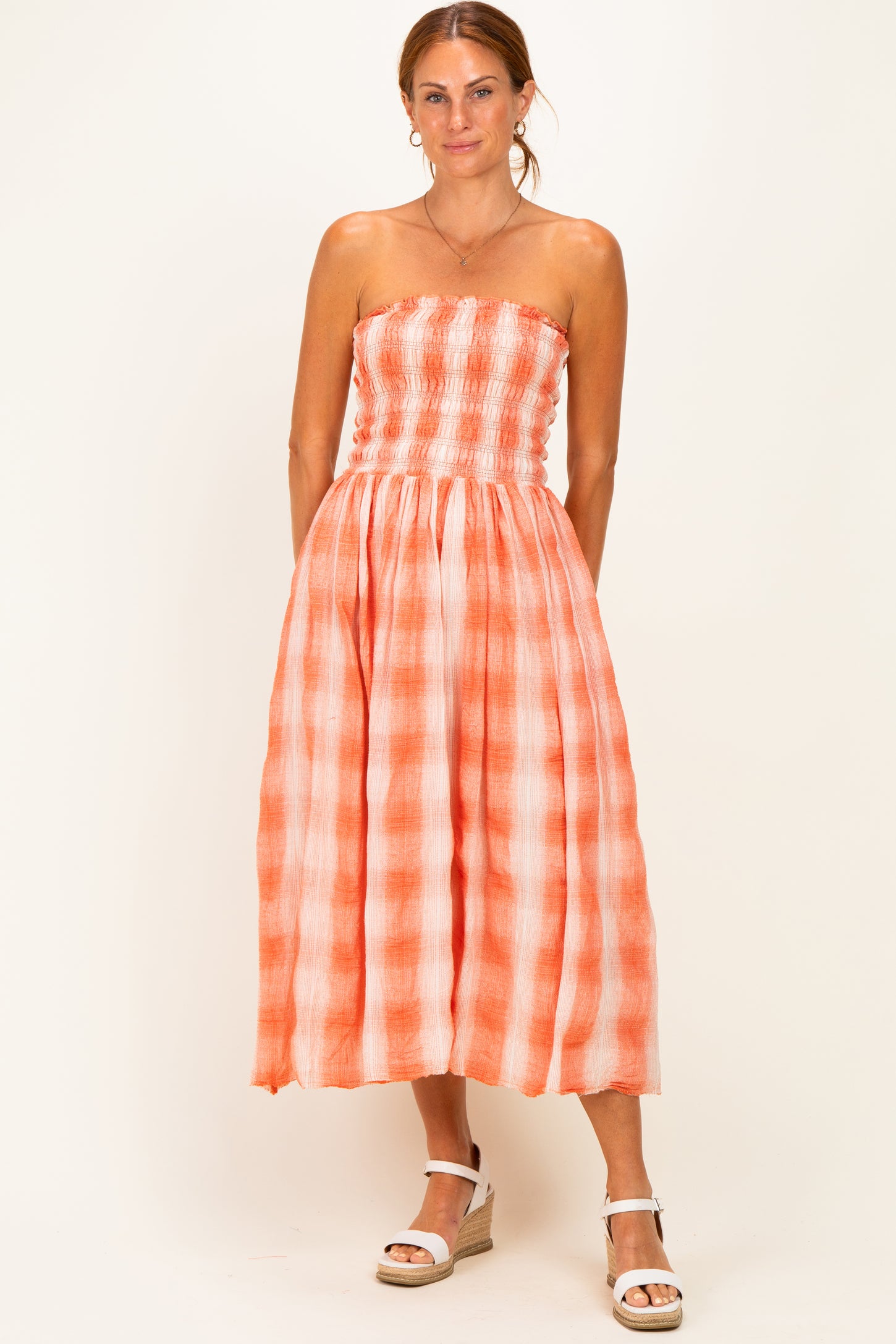 woman wearing an orange and white checkered strapless maxi dress with a smocked bodice and mid-calf length