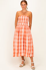 woman wearing an orange and white checkered strapless maxi dress with a smocked bodice and mid-calf length