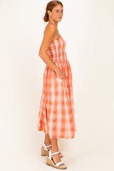 woman wearing an orange and white checkered midi dress with a smocked bodice and side pockets, styled with wedge sandals