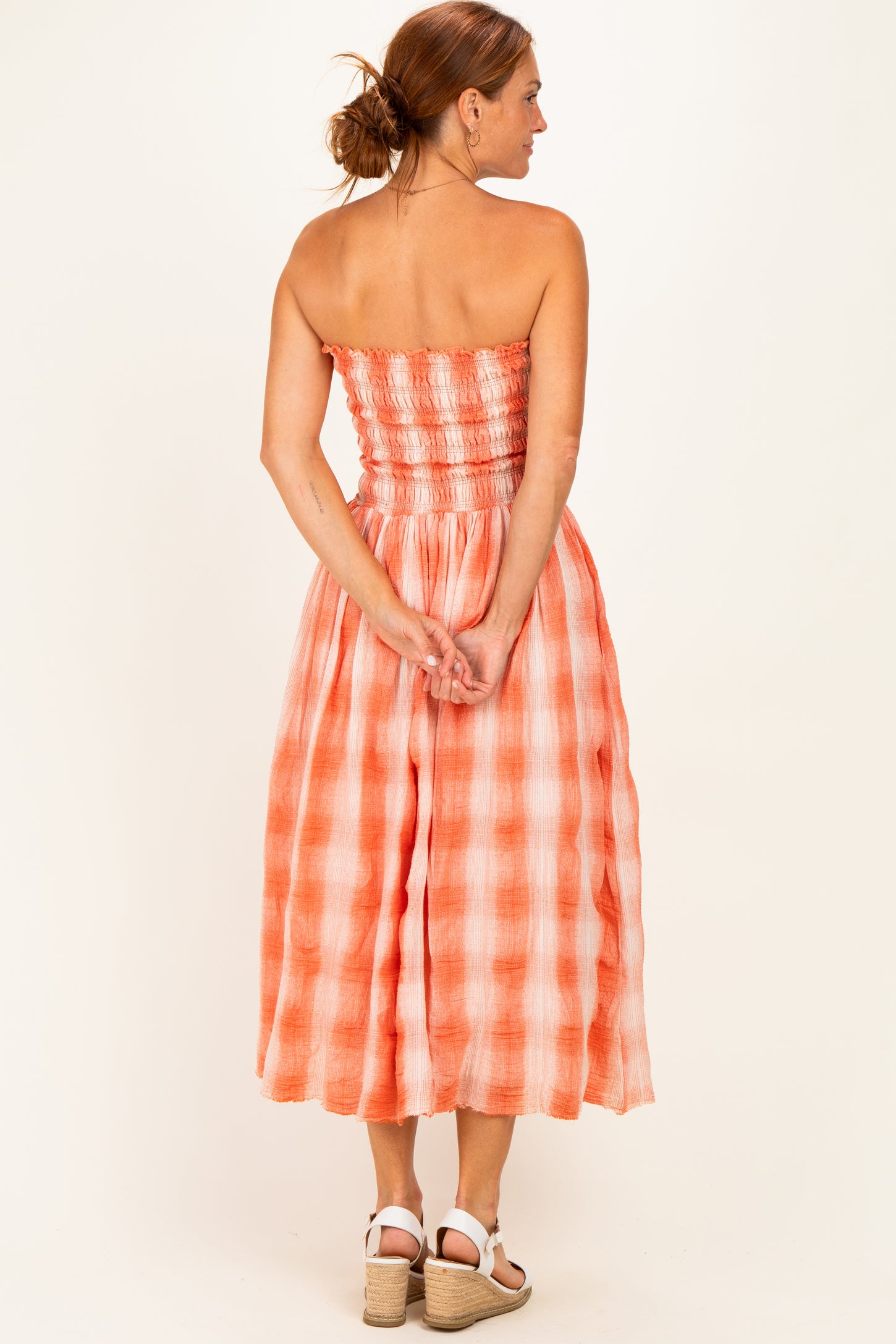 woman wearing an orange and white checkered strapless midi dress with a smocked bodice and a flowy skirt