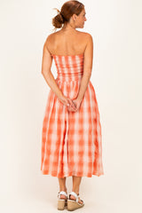 woman wearing an orange and white checkered strapless midi dress with a smocked bodice and a flowy skirt