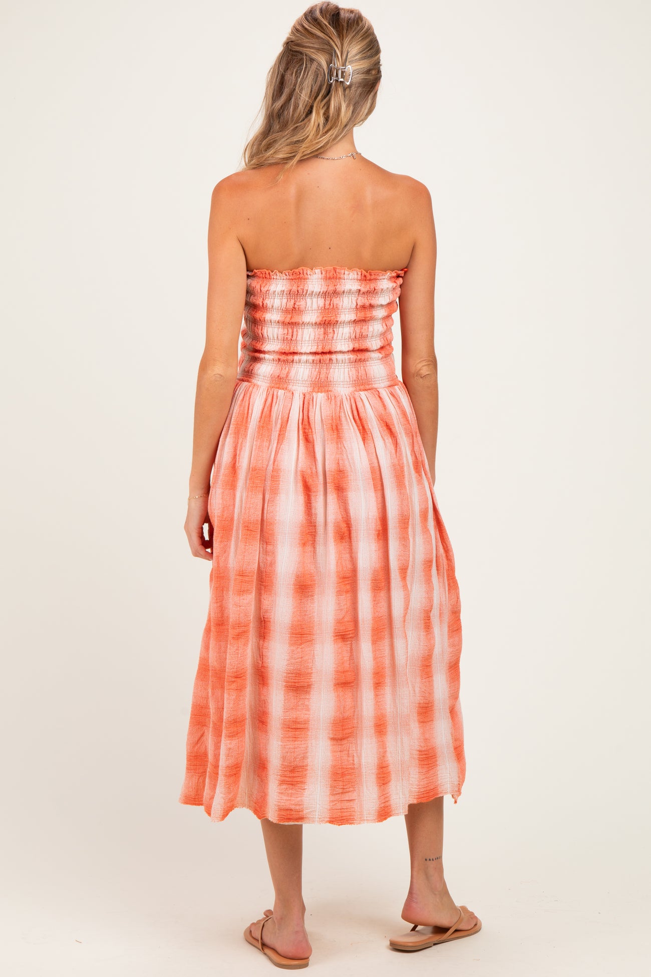 woman wearing a strapless orange checkered maternity dress, showing smocked bodice and flowing skirt from the back