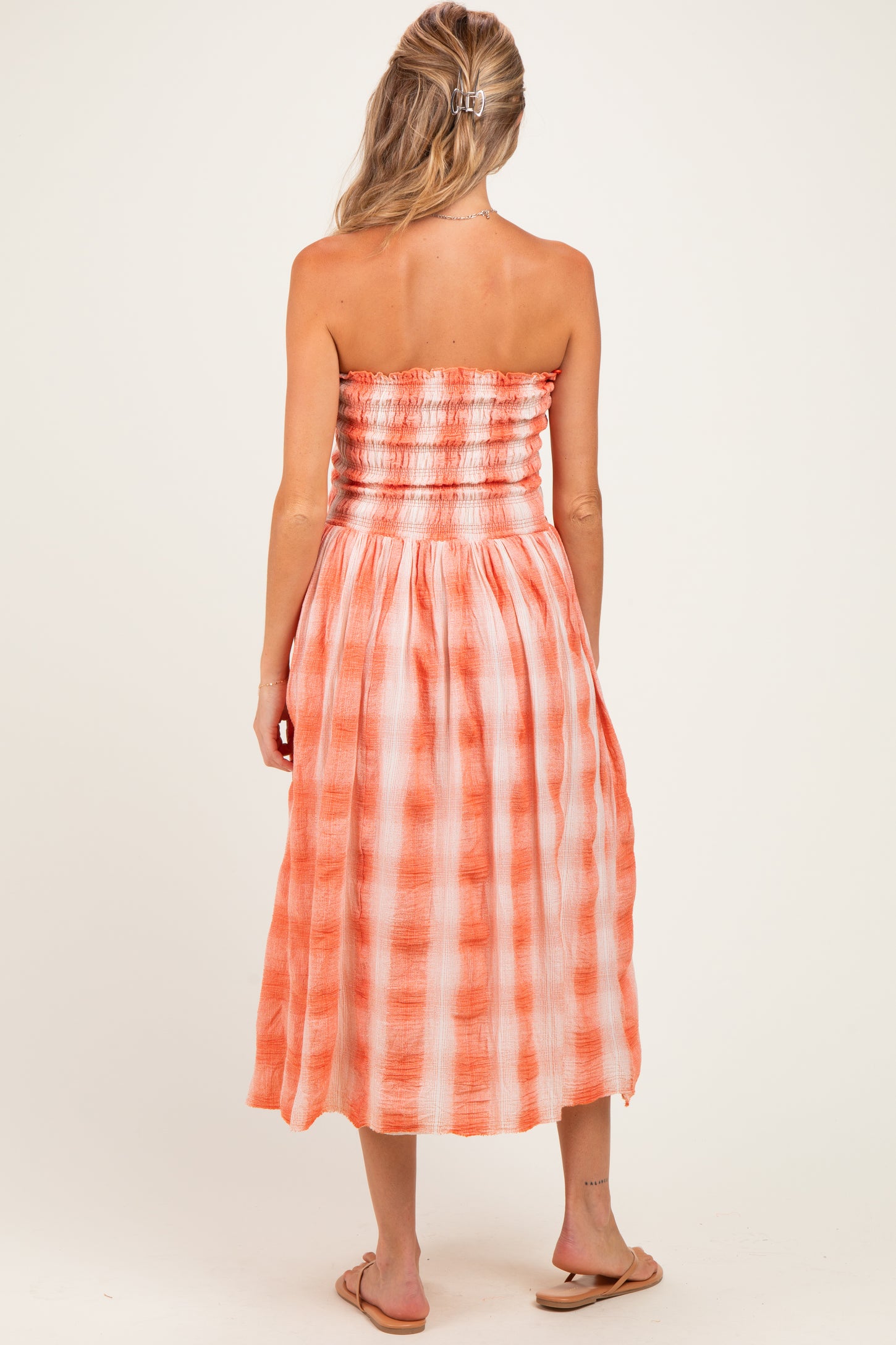 woman wearing a strapless orange checkered maternity dress, showing smocked bodice and flowing skirt from the back